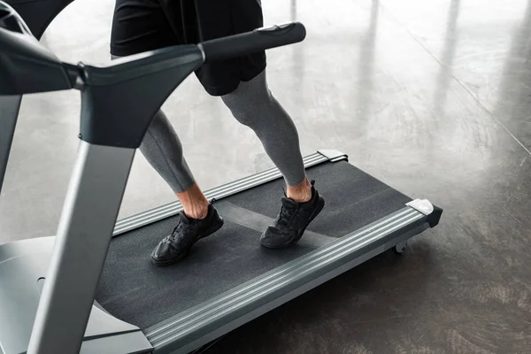 Niedriger Abschnitt des athletischen jungen Mannes in Sportbekleidung läuft auf dem Laufband in der Turnhalle — Stockfoto