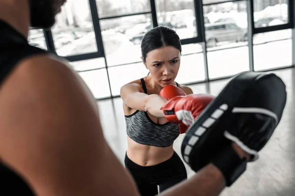 Cropped shot of male trainer exercising with young sportswoman in boxing gloves at gym — Stock Photo