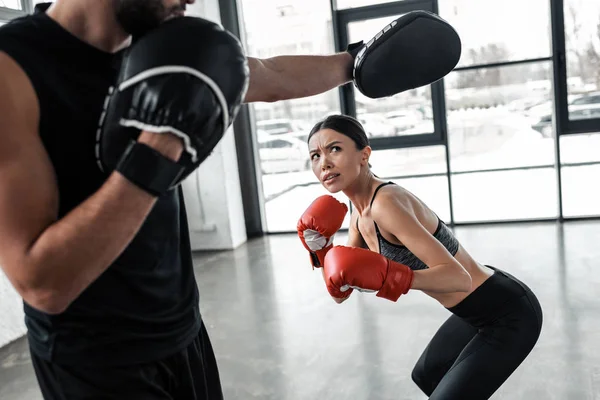 Cropped shot of male trainer exercising with sporty girl in boxing gloves at gym — Stock Photo