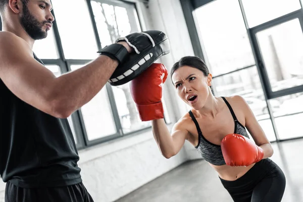 Агрессивная молодая спортсменка бокс и упражнения с тренером мужского пола в тренажерном зале — стоковое фото
