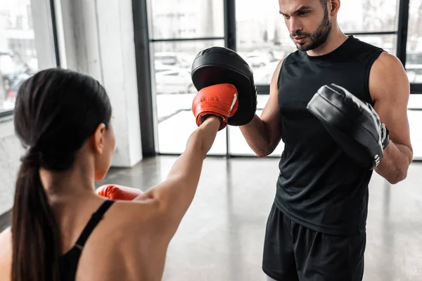 Cropped shot of male trainer and young sportswoman boxing in gym — Stock Photo