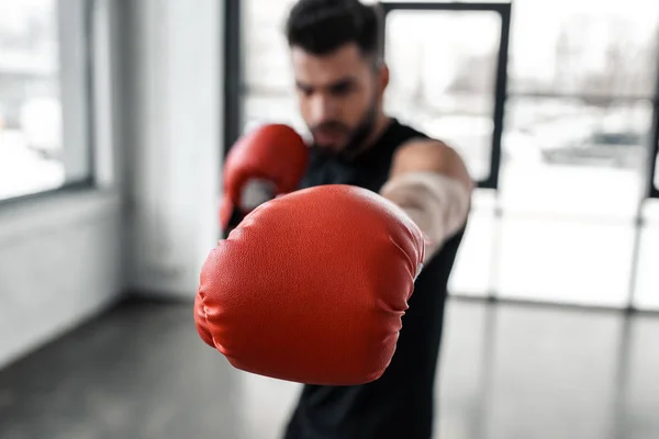 Close-up view of red boxing glove and young sportsman training in gym — Stock Photo
