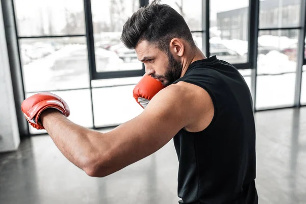 Vista lateral del guapo joven deportivo en el entrenamiento de guantes de boxeo en el gimnasio - foto de stock