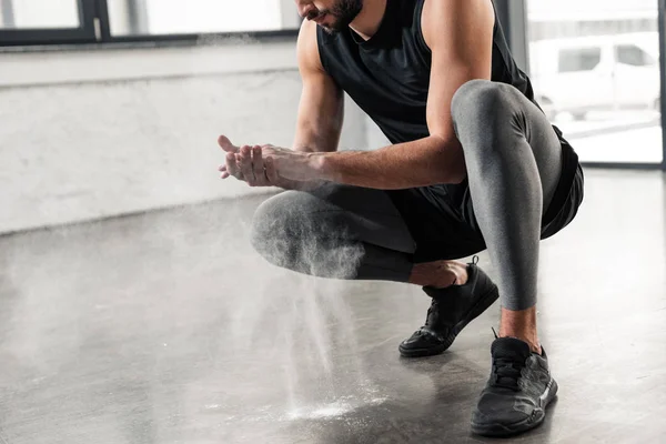 Cropped shot of young sportsman crouching and applying talcum powder on hands in gym — Stock Photo