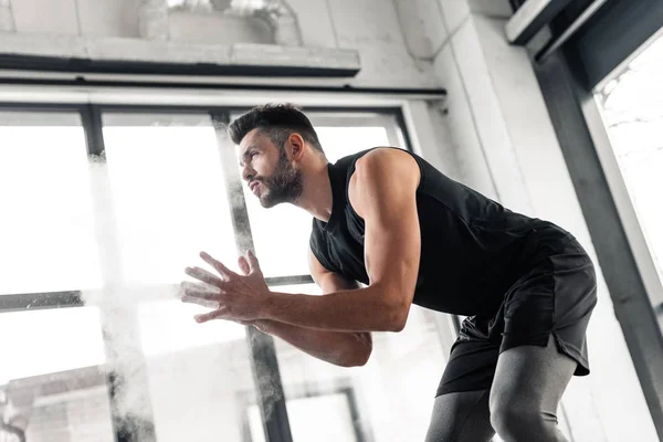 Tiefansicht eines athletischen jungen Mannes, der Talkumpuder auf die Hände aufträgt und im Fitnessstudio wegschaut — Stockfoto