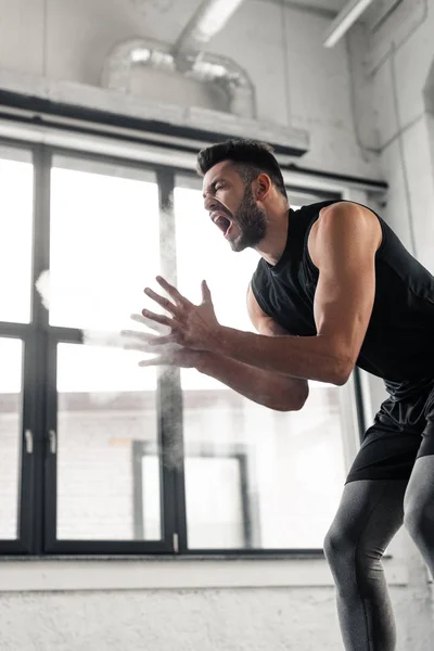 Sicht auf aggressive Sportler, die schreien und im Fitnessstudio Talkumpuder auf die Hände sprühen — Stockfoto