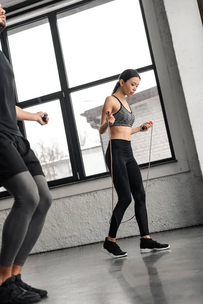 Cropped shot of young man and woman jumping with skipping ropes in gym — Stock Photo