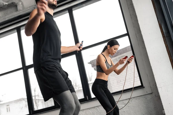 Corte tiro de jovem casal formação com pulando cordas no ginásio — Fotografia de Stock