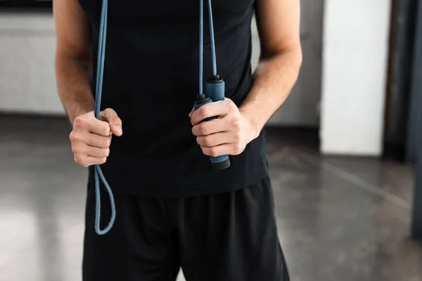 Section médiane de jeune homme athlétique en tenue de sport debout avec corde à sauter dans la salle de gym — Photo de stock