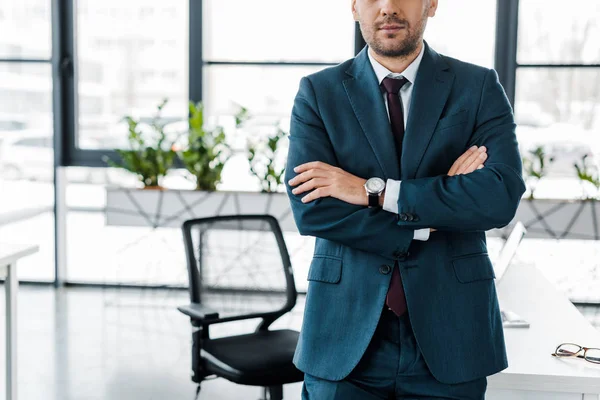 Vista ritagliata di uomo d'affari in piedi con le braccia incrociate in ufficio moderno — Foto stock