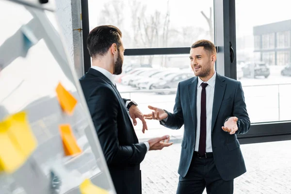 Messa a fuoco selettiva di bell'uomo d'affari che parla con il collega in ufficio moderno — Foto stock