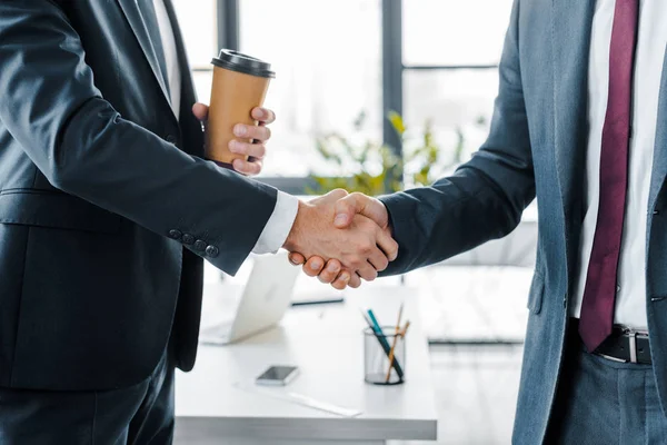 Abgeschnittene Ansicht von Geschäftsmann beim Händeschütteln während er Pappbecher im modernen Büro hält — Stockfoto