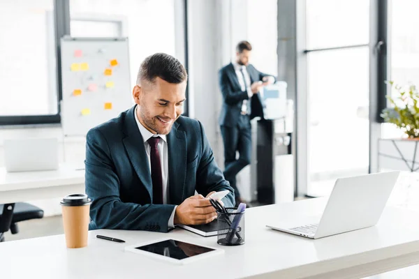 Cheerful businessman in formal wear looking at smartphone and smiling in modern office — Stock Photo