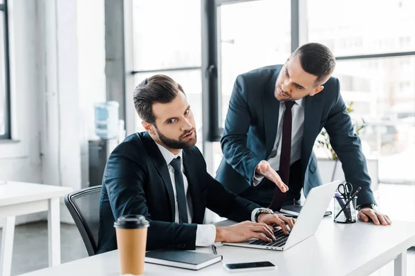 Enfoque selectivo de empresario insatisfecho escribiendo en el ordenador portátil cerca del hombre emocional en el desgaste formal - foto de stock