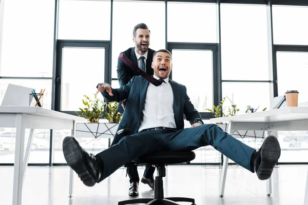 Homem de negócios feliz empurrando cadeira com colega animado no escritório moderno — Fotografia de Stock