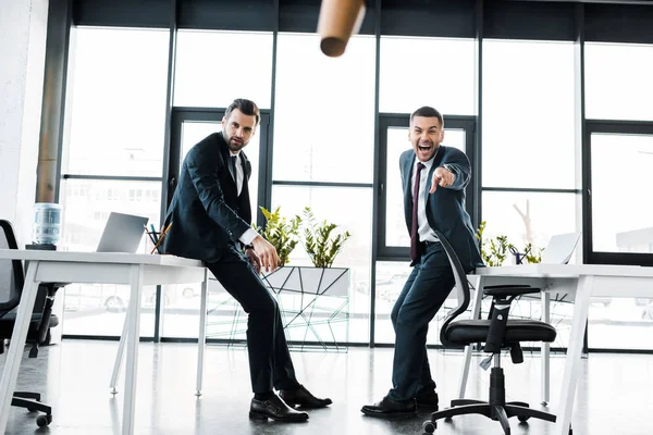 Fröhlicher Geschäftsmann in formeller Kleidung zeigt mit dem Finger auf fallenden Pappbecher in modernem Büro — Stockfoto