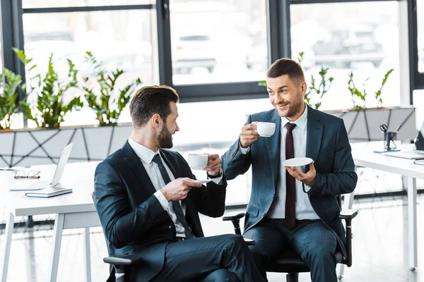 Gut aussehende Männer in Formaltracht reden, während sie Tassen mit Getränken in der Hand halten — Stockfoto