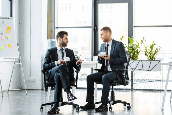 Handsome businessmen talking while holding cups with drinks — Stock Photo