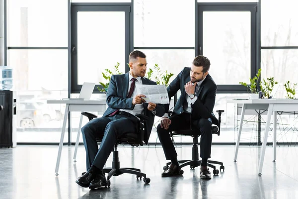 Homens de negócios bonitos lendo jornal de negócios enquanto sentados no escritório moderno — Fotografia de Stock