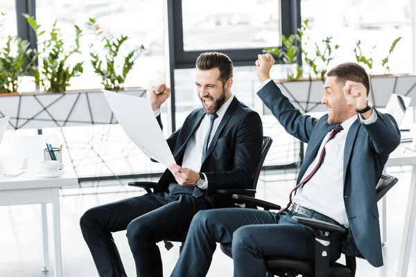 Fröhliche Geschäftsleute schauen auf Papier und feiern den Sieg im modernen Büro — Stockfoto