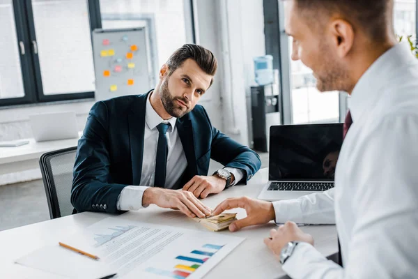 Uomo d'affari che dà banconote in dollari al collega in ufficio moderno — Foto stock