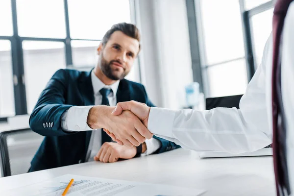 Enfoque selectivo de apretón de manos de los hombres de negocios en la oficina moderna - foto de stock