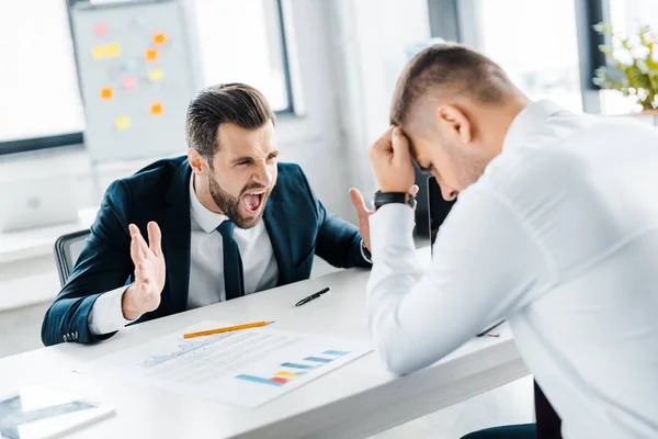 Enfoque selectivo de hombre enojado en desgaste formal gritándole a su compañero de trabajo en la oficina moderna — Stock Photo