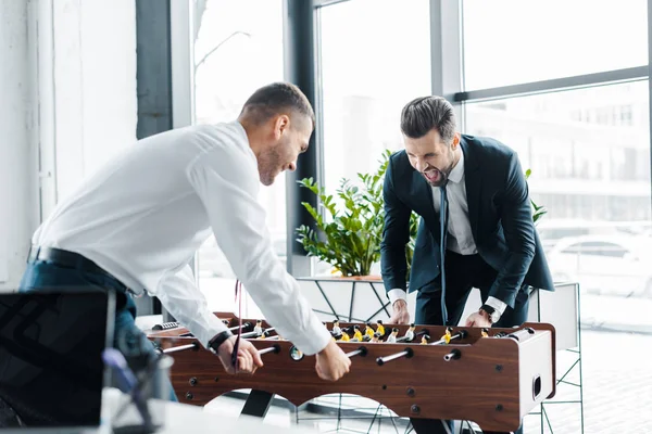 Hombres de negocios felices jugando fútbol de mesa en la oficina moderna - foto de stock