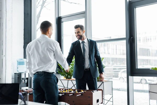 Happy businessmen shaking hands near table football in modern office — Stock Photo