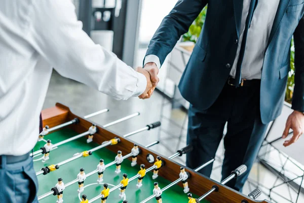 Vista cortada de empresários apertando as mãos perto de futebol de mesa — Fotografia de Stock