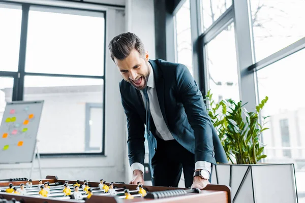 Excited bearded businessman in formal wear playing table football — Stock Photo