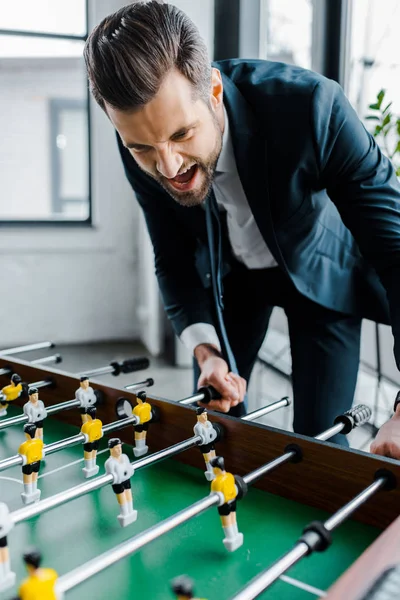 Felice uomo d'affari barbuto in abbigliamento formale giocare a calcio balilla — Foto stock