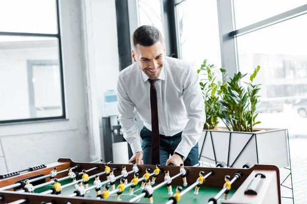 Sonriente hombre de negocios en ropa formal jugando futbolín - foto de stock