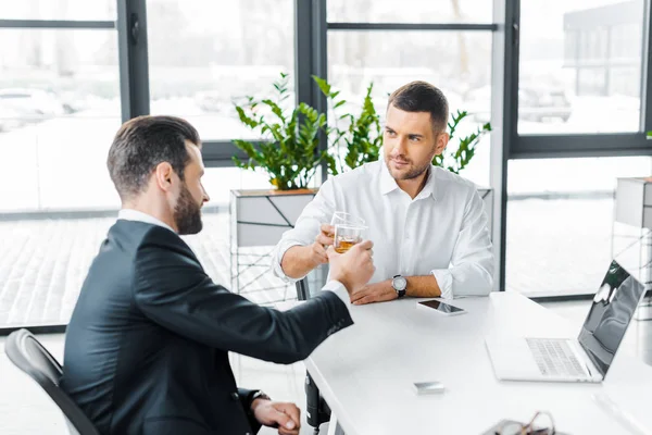 Handsome businessmen holding alcohol drinks in hands while sitting in modern office — Stock Photo