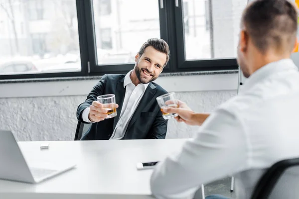 Alegre hombre de negocios sosteniendo vaso de whisky mientras mira a su compañero de trabajo - foto de stock