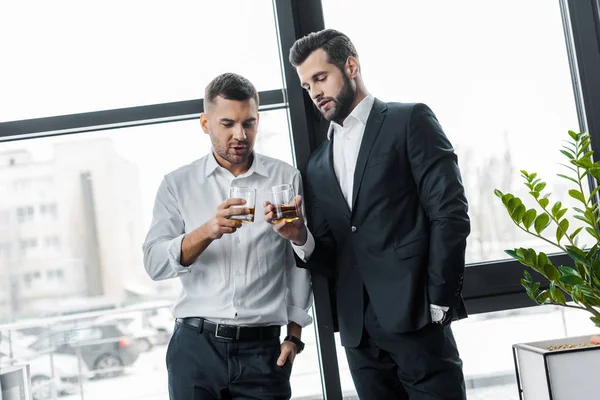 Hombres de negocios de pie con las manos en los bolsillos mientras sostiene vasos con bebidas alcohólicas - foto de stock