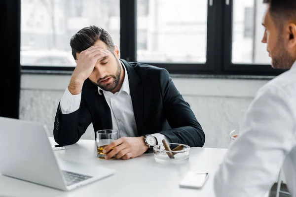 Selektiver Fokus müder Geschäftsleute mit Kopfschmerzen beim Halten von Glas mit Alkoholgetränk im modernen Büro — Stockfoto