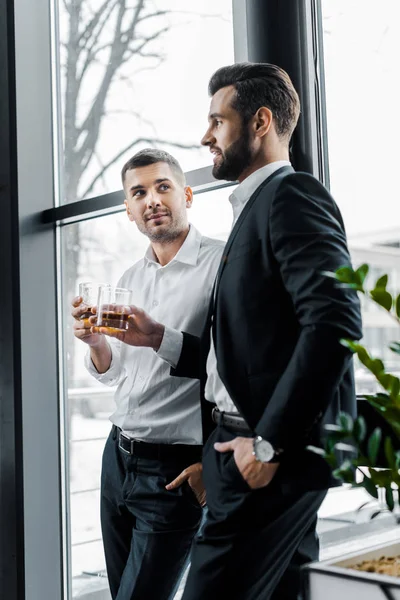 Businessmen standing with hands in pockets and holding glasses with alcohol drinks — Stock Photo