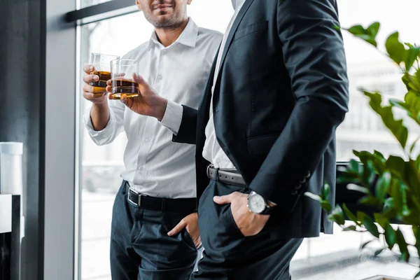 Vista cortada de empresários de pé com as mãos nos bolsos e segurando óculos com bebidas alcoólicas — Fotografia de Stock