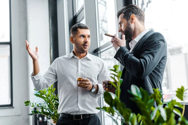 Geschäftsmann hält ein Glas Whiskey in der Hand und diskutiert mit Mitarbeiter mit kubanischer Zigarre in der Hand — Stockfoto