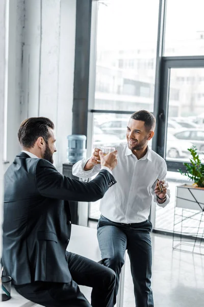 Felices hombres de negocios brindando con vasos de whisky - foto de stock