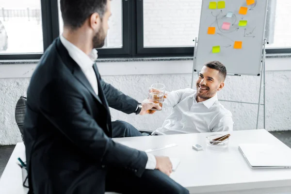 Веселий бізнесмен смердить алкогольним напоєм у склянці з колегою в сучасному офісі — стокове фото