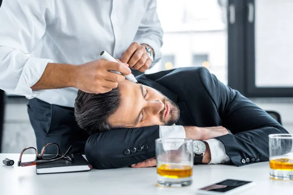 Vista recortada del hombre sosteniendo marcador cerca de dormir compañero de trabajo en la oficina moderna - foto de stock