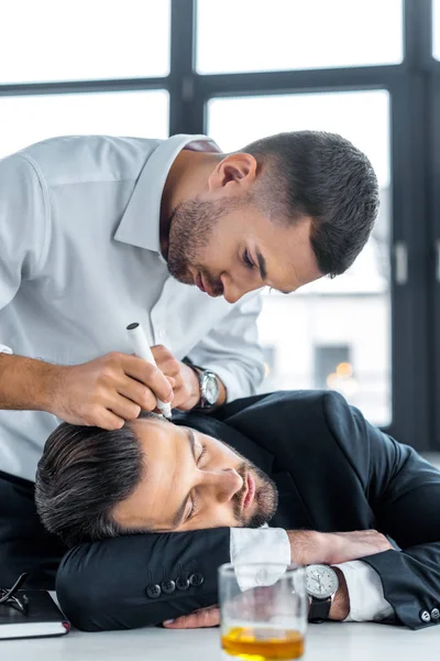 Man drawing with marker on face of sleeping coworker in modern office — Stock Photo