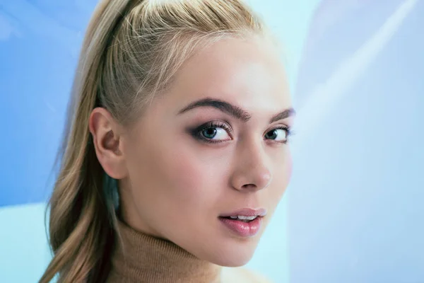 Mujer rubia bonita mirando a la cámara con interés en el fondo azul - foto de stock