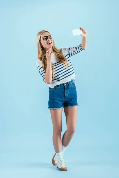 Visão de comprimento total da mulher rindo fazendo selfie com óculos de brinquedo no fundo azul — Fotografia de Stock