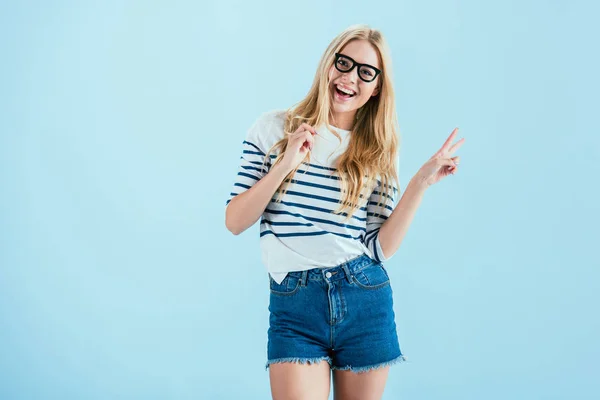 Studio shot of joyful girl holding toy glasses and showing peace sign on blue background — Stock Photo