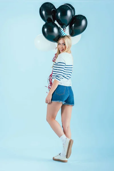 Excited girl with bunch of party balloons looking over shoulder on blue background — Stock Photo