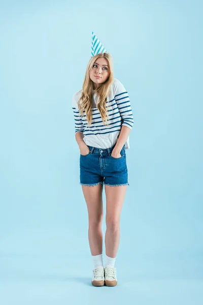 Long-haired girl in party hat posing with hands in pockets on blue background — Stock Photo