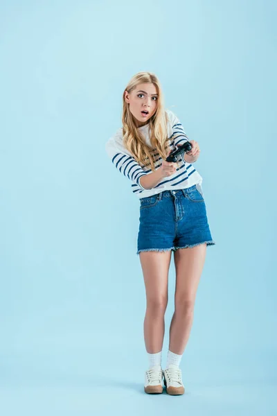 Überrascht blondes Mädchen posiert mit Spielcontroller auf blauem Hintergrund — Stockfoto